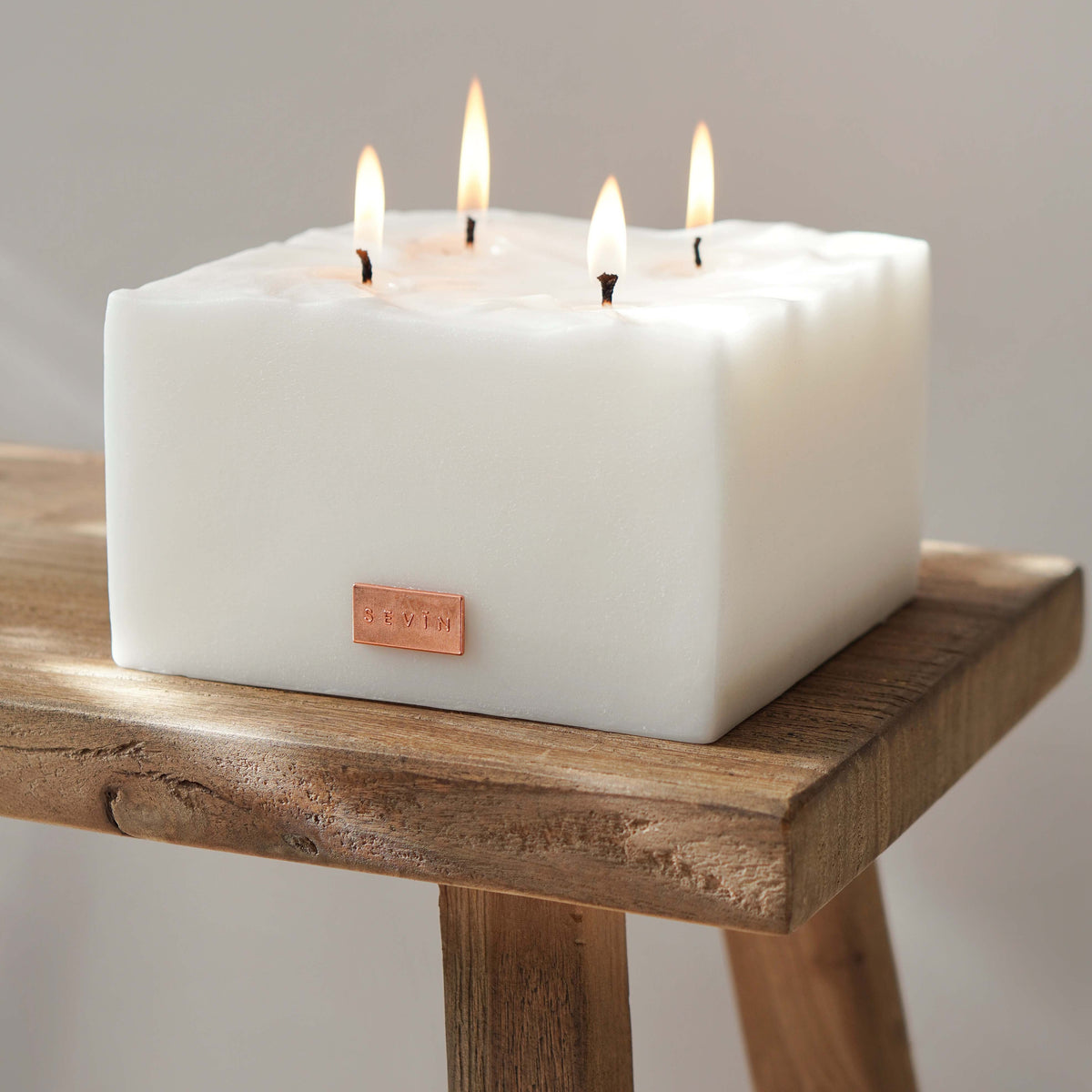 Square white SEVIN candle with four wicks on a wooden stand against a plain background - Porcelain White Scented Candle
